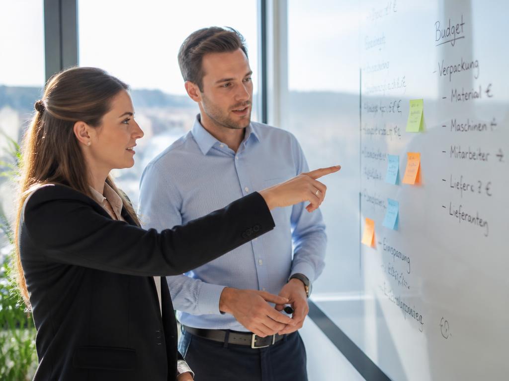 Zwei Personen analysieren gemeinsam einen Workflow auf einem großen Digital-Board